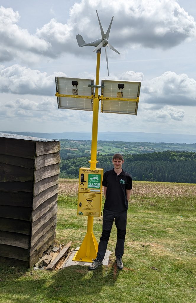 Mike Dowson, founder and Managing Director of Turtle with an installed solar and wind powered defib cabinet at Kington Golf Club in Hereford