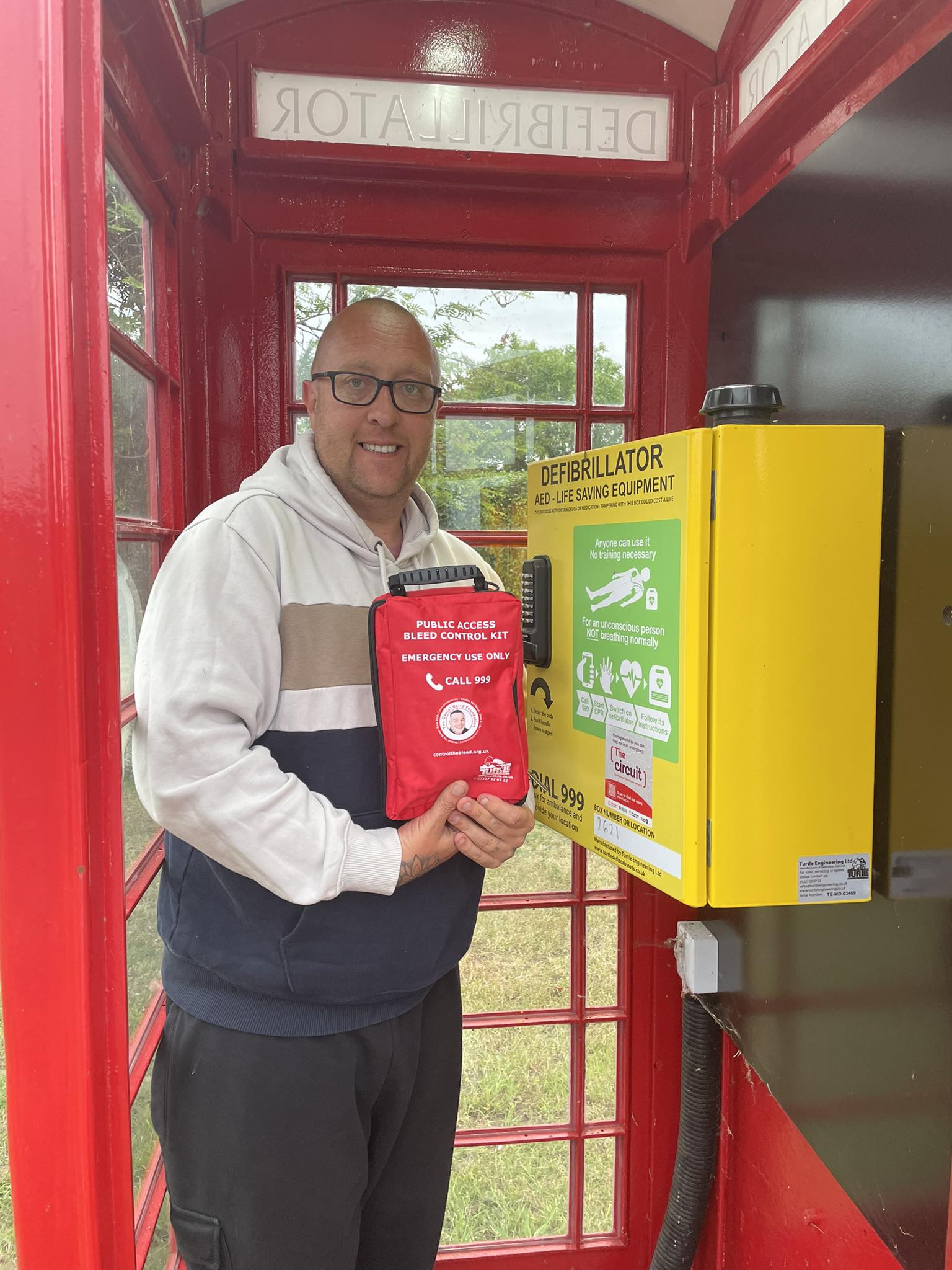 Kyle Hotchkins showing bleed control kit and Turtle defibrillator cabinet installed in public phone box 
